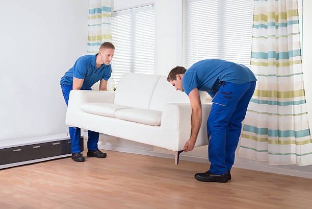 full length of male movers placing sofa on hardwood floor at home